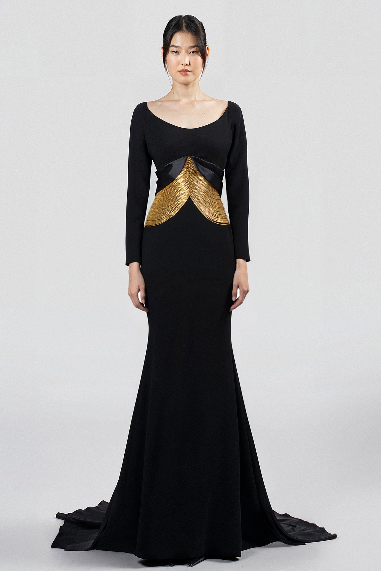 Load and play video in Gallery viewer, Floor-length dress, black crepe bodice, long sleeves, scoop neckline, fitted silhouette, mermaid skirt with satin train, gold embroidered V-shape silene design at waist.